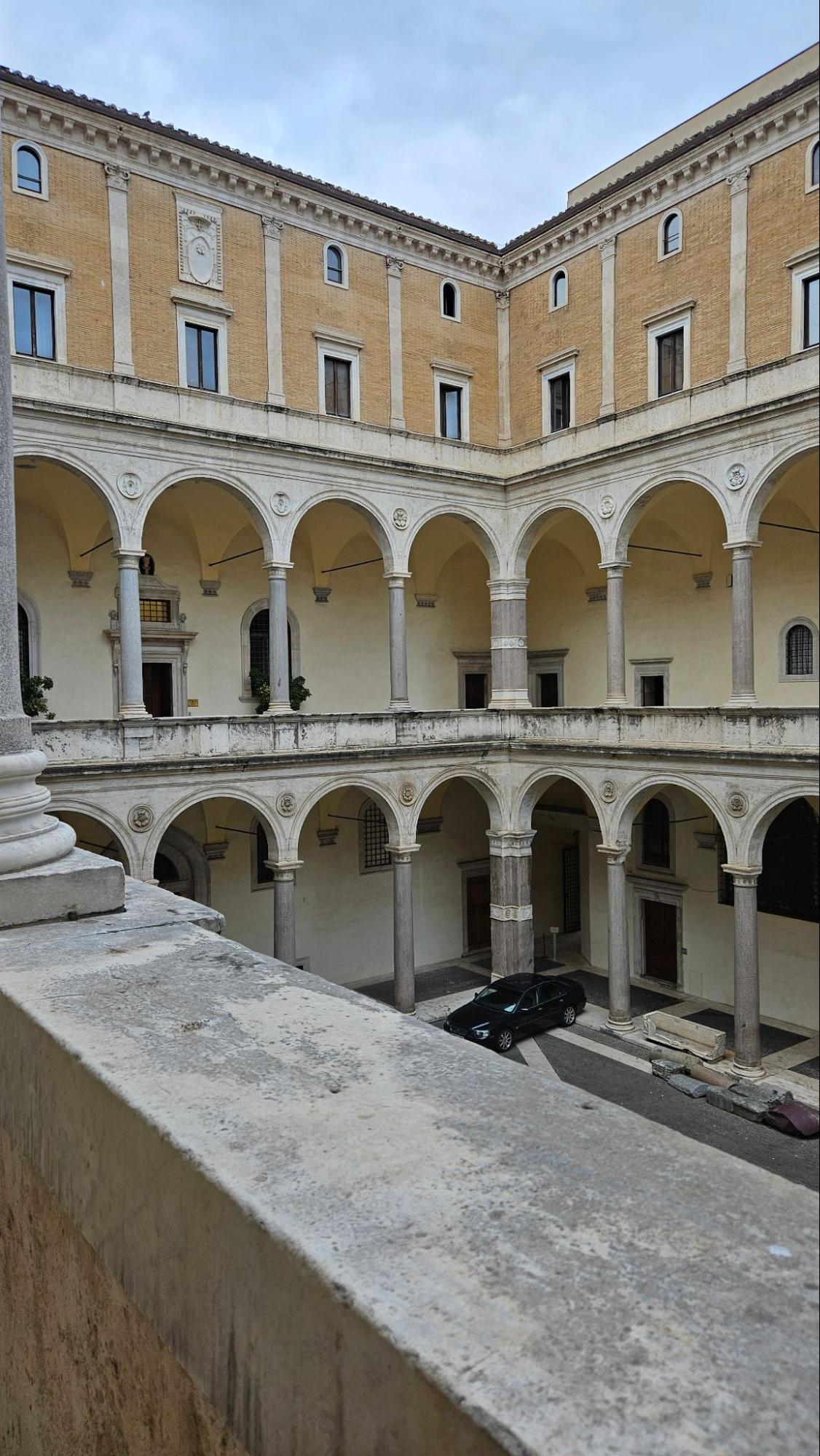 Kuvassa näkyy Rooman keskustassa sijaitseva Palazzo della Cancellerian sisäpiha. Kivinen rakennus on erittäin mahtipontinen ja tyylitelty. Komeat marmoriset pylväsrivit koristeluineen lisäävät ylellisyyden tuntua. Kahdessa alemmassa kerroksessa voi kulkea pylväskäytäviä, mutta kaksi ylempää kerrosta ovat tiiliverhoiltua julkisivua isoine ja pienine ikkunoineen.