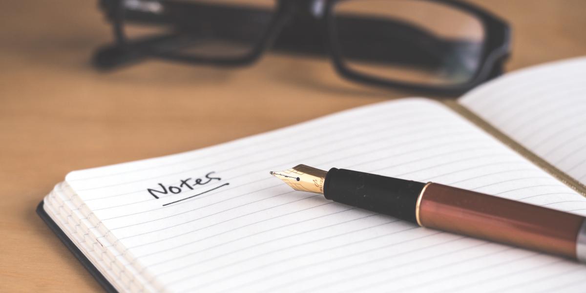 A notebook, a pen and glasses on a table.