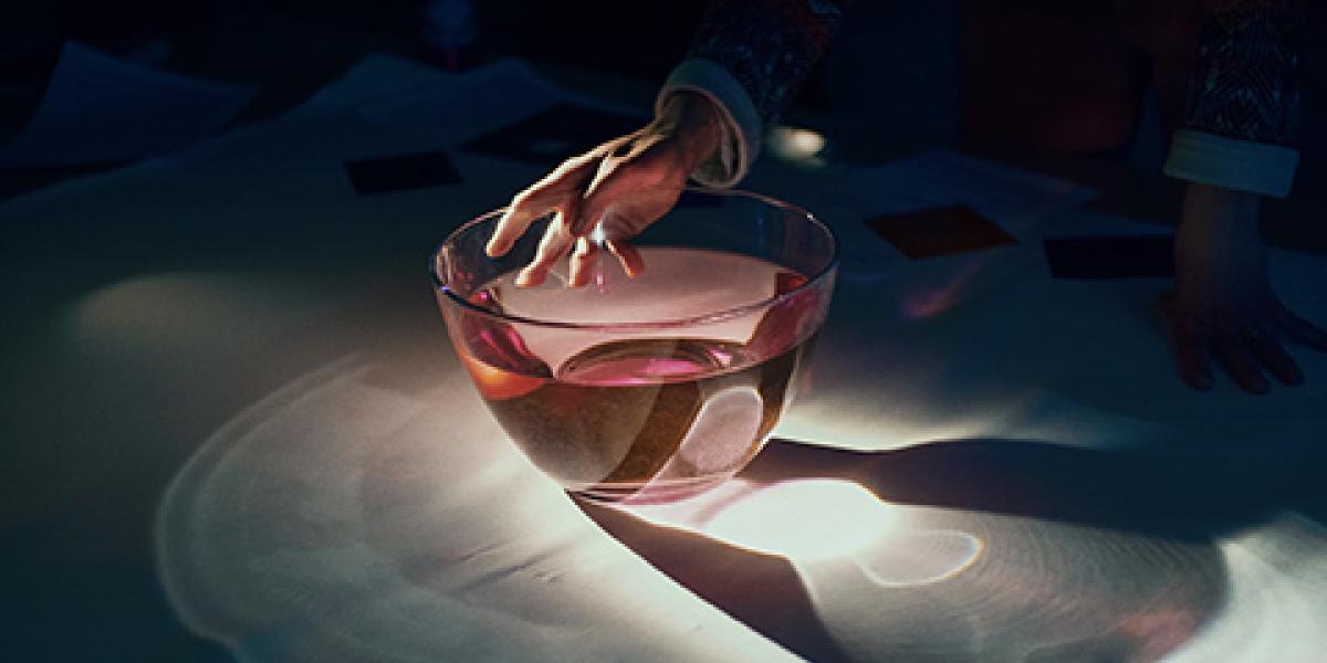 Kuvituskuva, Kädessä pidetty lasimalja heijastuu pöydälle.