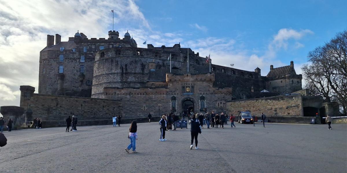 Edinburgh castle on a sunny day with several people on the yard. The castle is built on a cliff in central Edinburgh.iolle rakennettu linna Edinburghin keskustassa. 