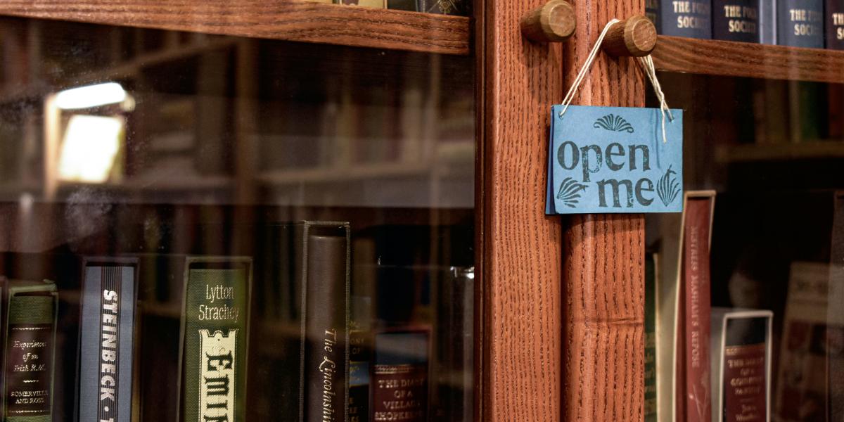 Kuvituskuva. Lasinen kirjakaappi, jossa lukee "open me". 