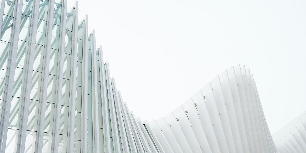 Fotografi av en välvd byggnad med raka, ljusa balkar mot vitgrå himmel..
