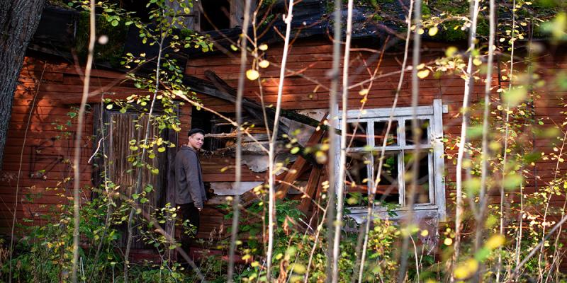 Ville-Juhani Sutinen seisoo hylätyn punaisen talon ovella kääntyneenä kameraan.